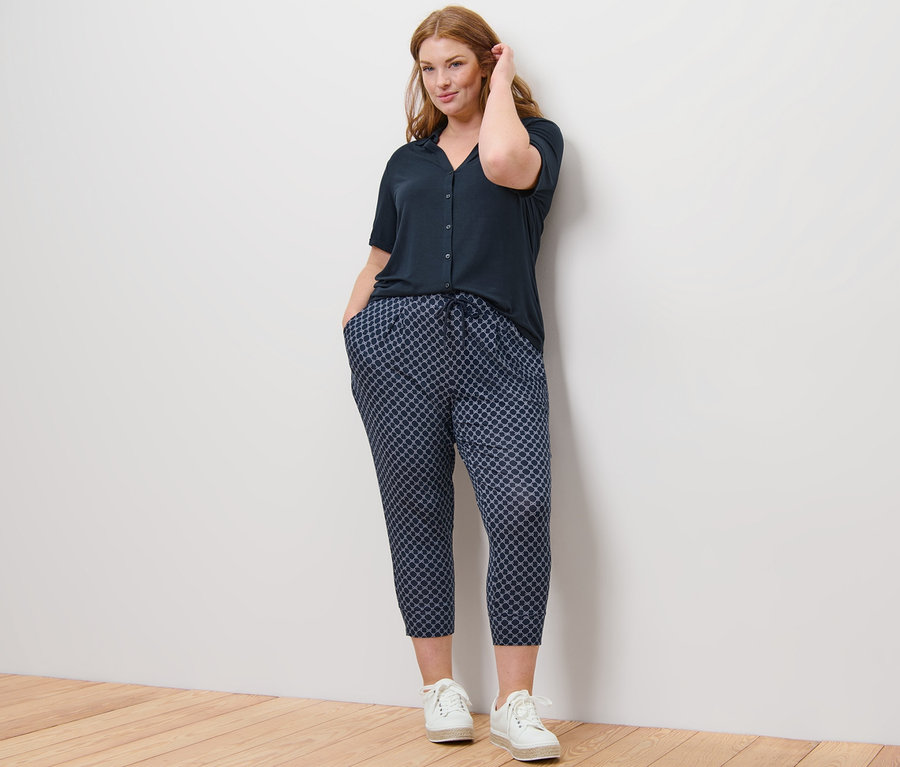 Femme posant en blouse bleu foncé avec patte de boutonnage et pantalon 3/4 en jersey imprimé.