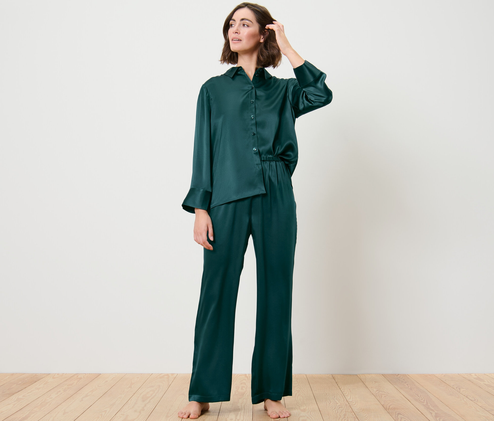 Une femme porte un pantalon de pyjama en soie et pose dans une pièce.