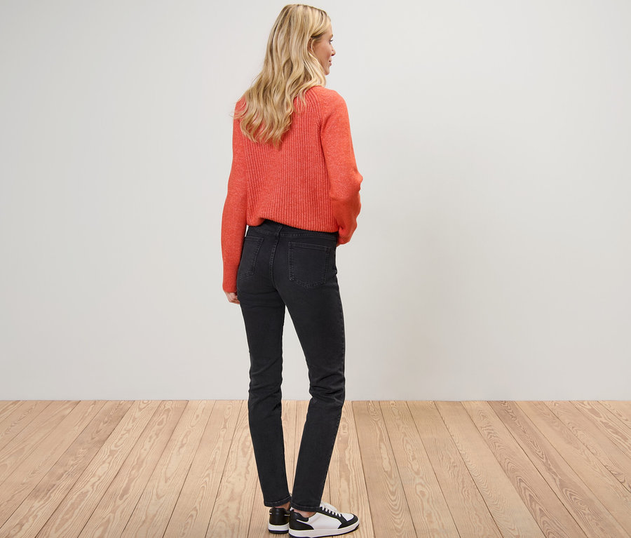 Une femme blonde pose de dos, portant un pull orange et un Jean Slim – Fit « Emma ».