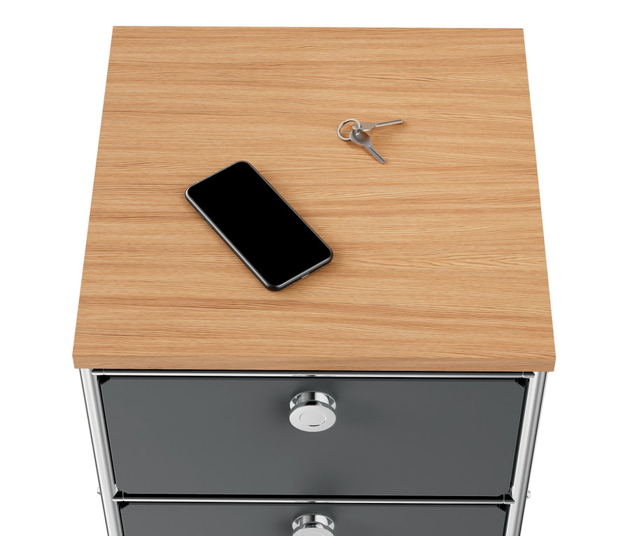 Sur la commode étroite en métal gris « CN3 » avec plateau en bois et 2 tiroirs reposent un téléphone et des clés.