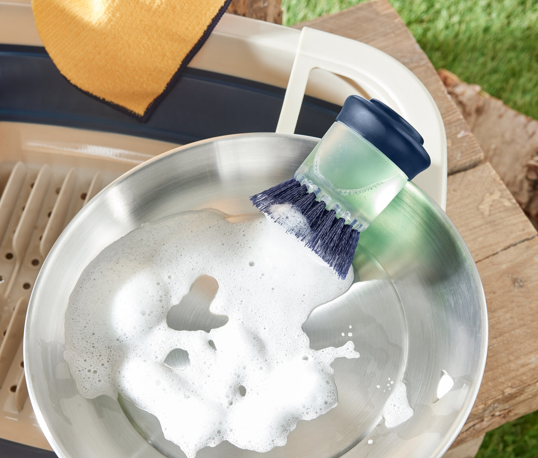 Une poêle en acier inoxydable est lavée avec une brosse avec distributeur. À côté se trouvent un égouttoir et un chiffon.