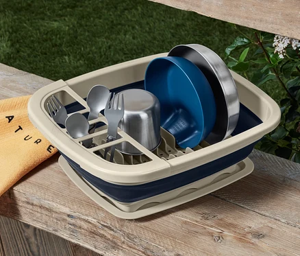 Égouttoir pliable avec vaisselle et couverts sur une table en bois.
