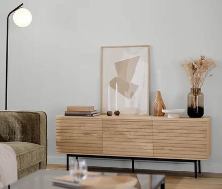 Un canapé 3 places en velours côtelé marron-gris, un lampadaire noir avec un globe en verre, un meuble bas et un lot de deux tables basses dans un salon.