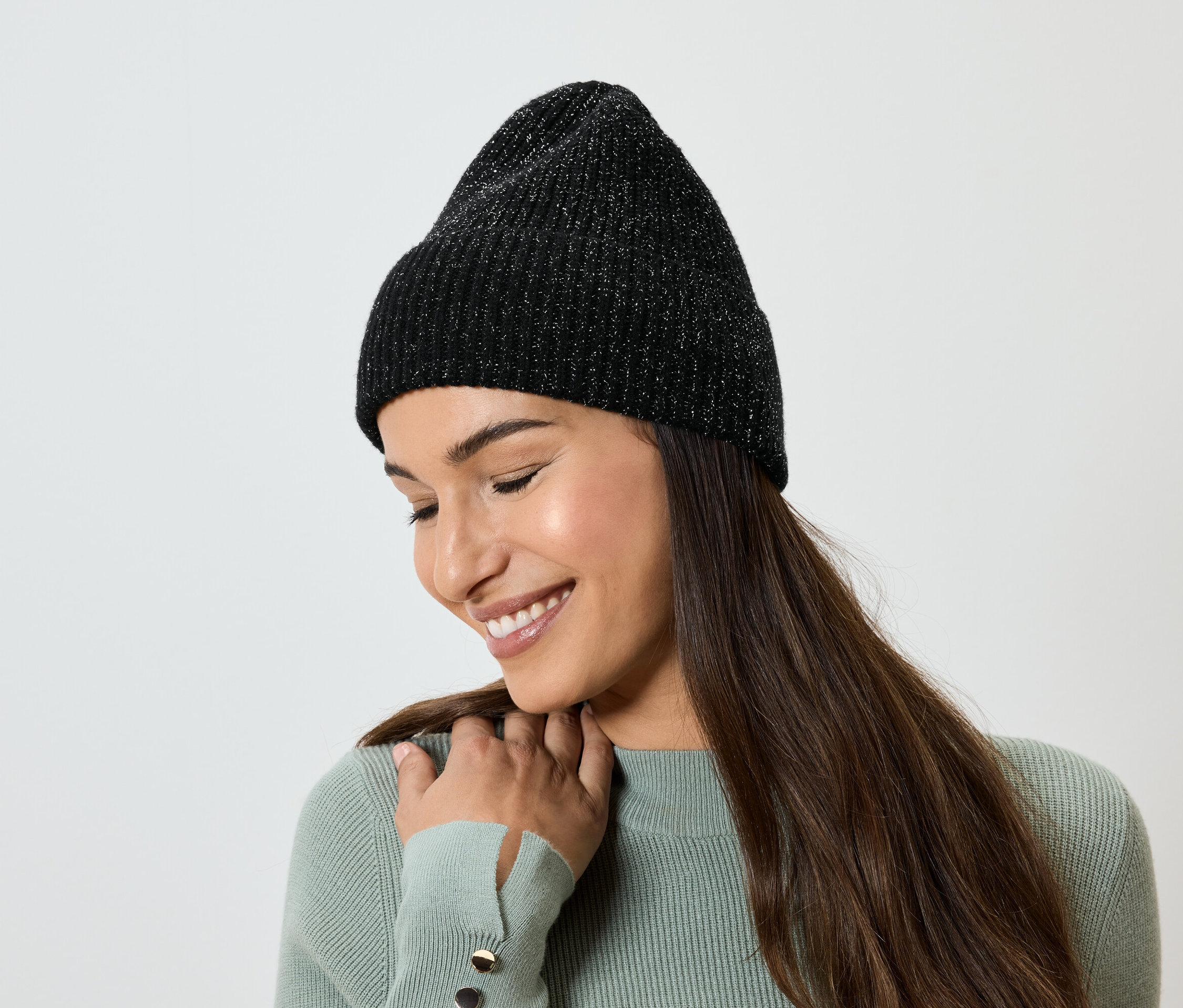 Une femme aux longs cheveux bruns sourit et porte un bonnet en tricot noir.