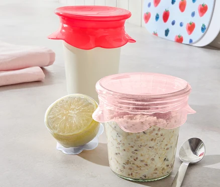 Deux verres avec du contenu sont recouverts de 3 couvercles en silicone. À côté se trouvent un citron et une cuillère.