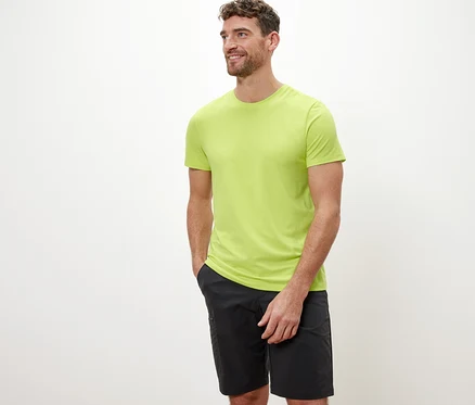 Un homme aux cheveux bruns pose sur un fond blanc portant un t-shirt technique lime.
