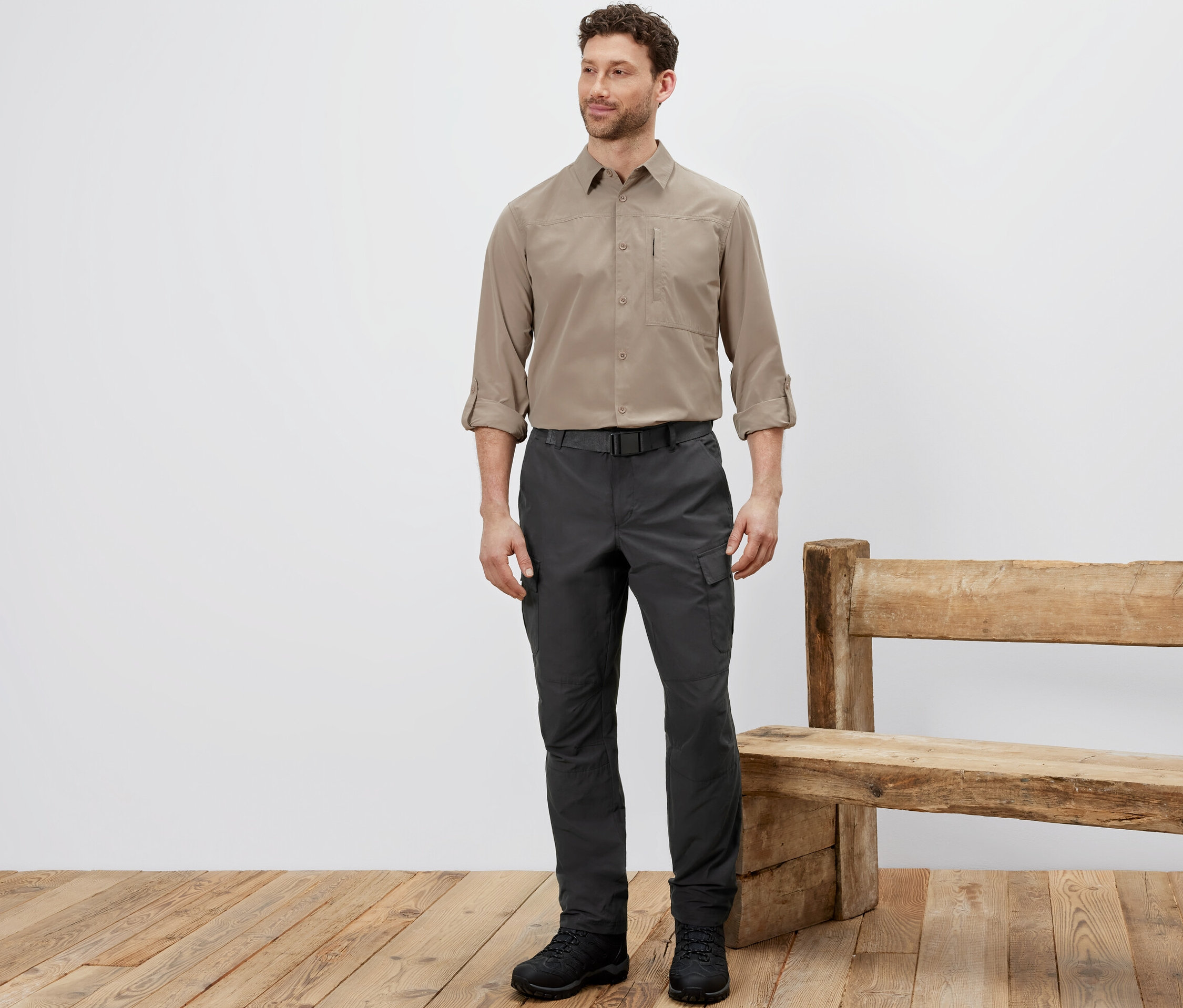 Un homme debout porte un pantalon d’extérieur avec protection anti-moustiques, une chemise beige et des chaussures noires.