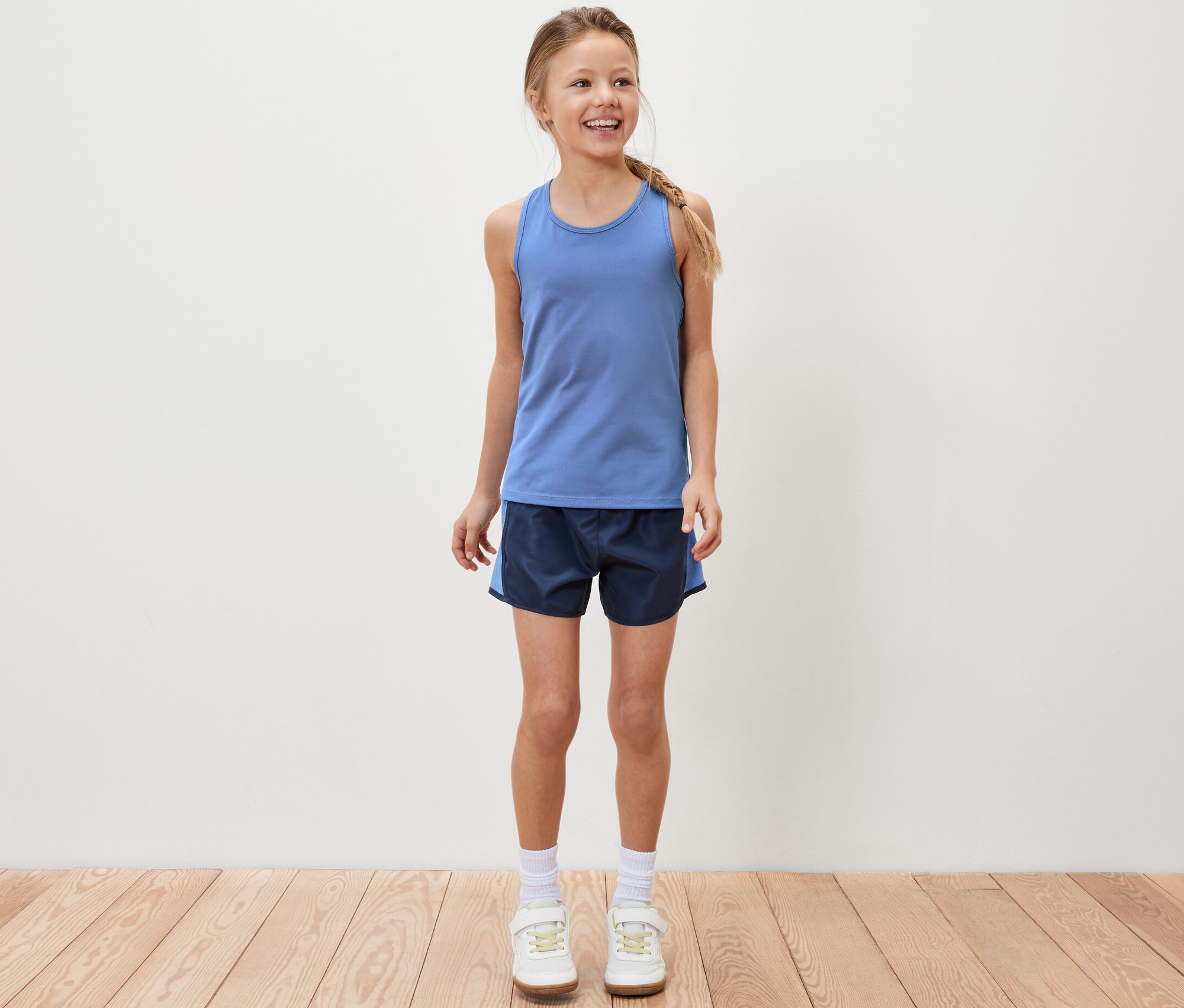 Une fille souriante est debout et porte un débardeur de sport bleu et un short de sport.
