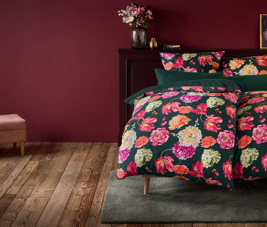 Linge de lit à fleurs sur lit avec table de chevet, lampe et banc rose.