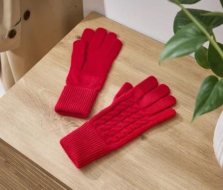 Deux gants tricotés rouges sont posés sur une table en bois à côté d'une plante dans un pot blanc.