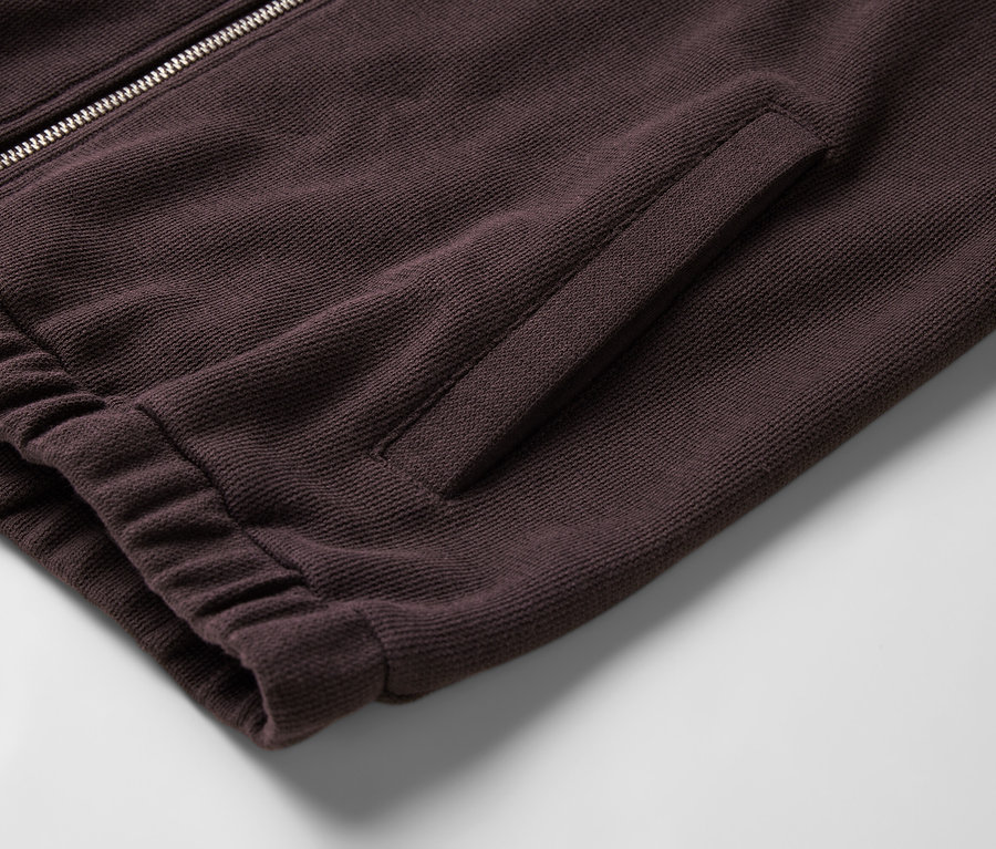 Détail d'un sweat-shirt bordeaux zippé avec une poche et une bordure côtelée.