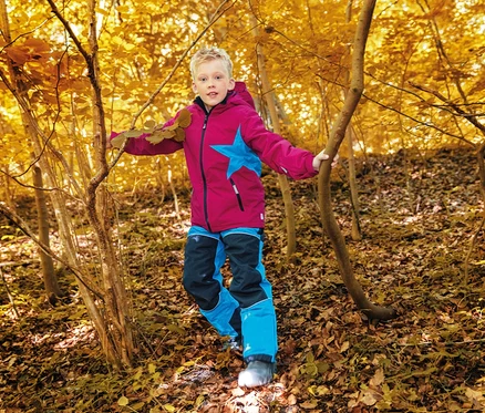 Un garçon vêtu d'une veste rose avec une étoile bleue et d'un pantalon bleu et noir marche dans une forêt d'automne.