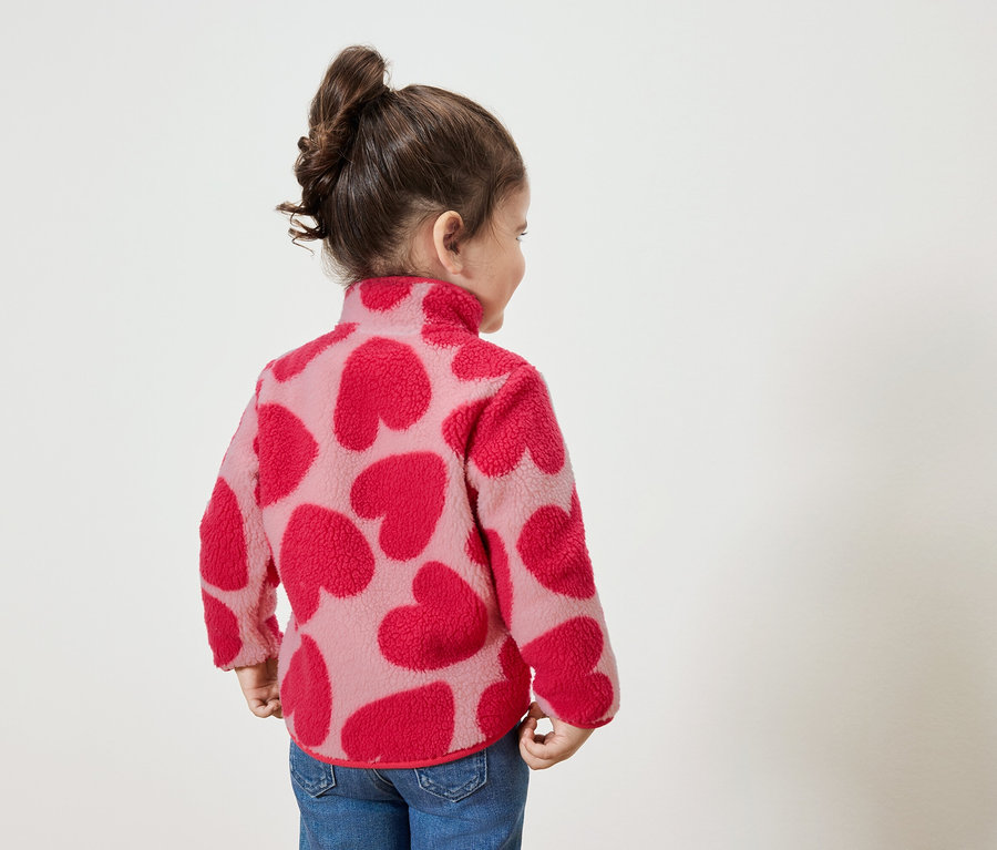 Petite fille portant un sweat-shirt à motifs de cœurs rouges, regardant vers la droite.