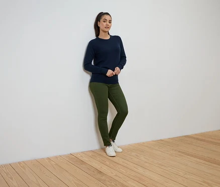Une femme se tient contre un mur, portant un pull bleu marine, un jean vert et des baskets blanches.