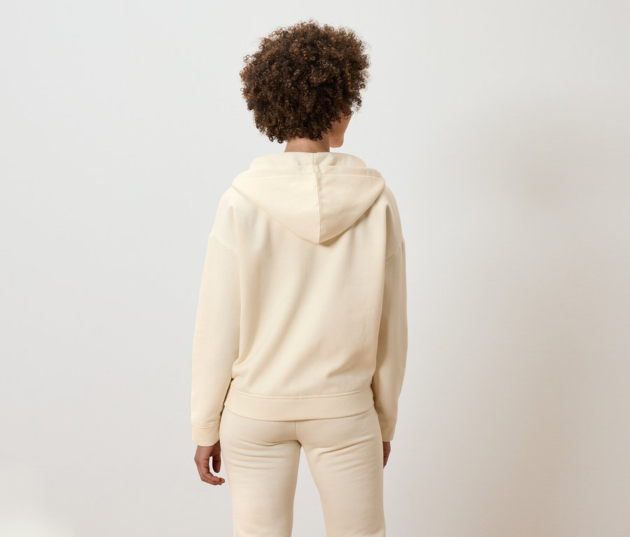 Vue arrière d'une femme aux cheveux bouclés portant un ensemble beige à capuche.