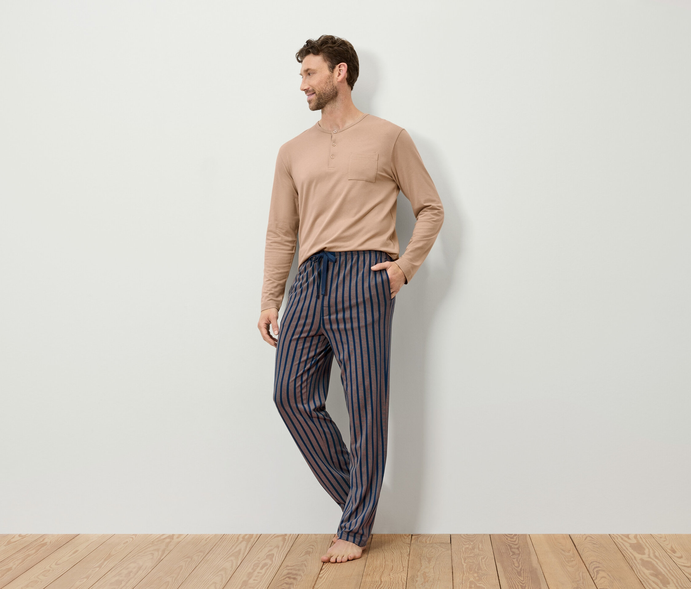 Un homme portant un haut de pyjama beige à manches longues et un pantalon de pyjama rayé.