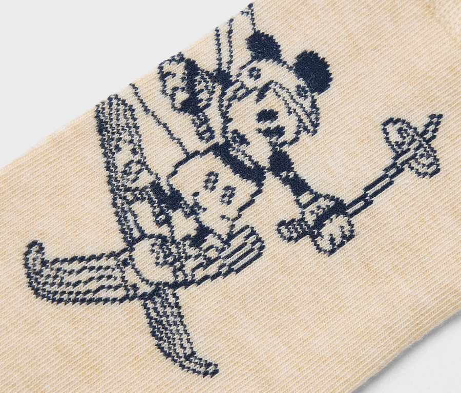 Gros plan d'une chaussette beige avec un motif bleu foncé de Mickey Mouse faisant du ski.