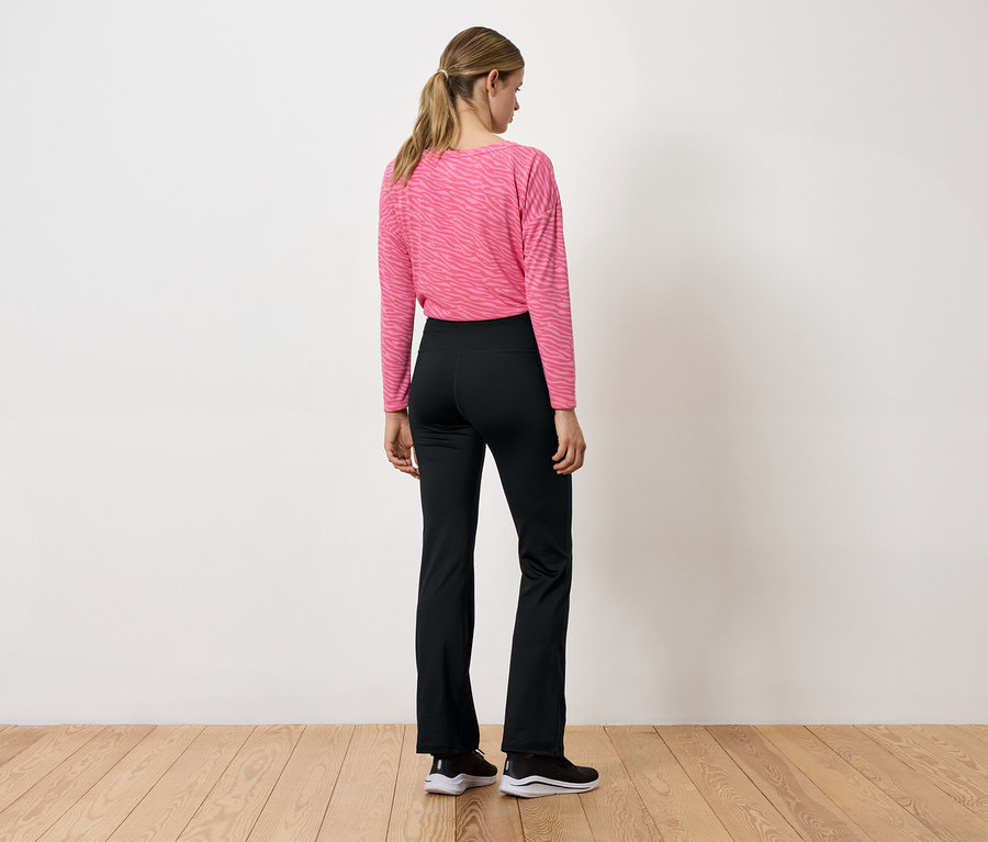 Une femme, dos à la caméra, porte un haut rose à manches longues et un pantalon noir.