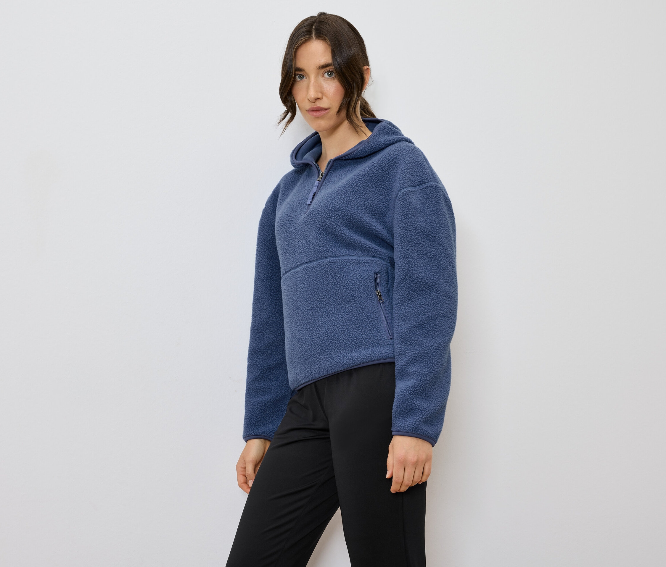 Femme posant portant un sweat à capuche en polaire bleu et un pantalon noir.