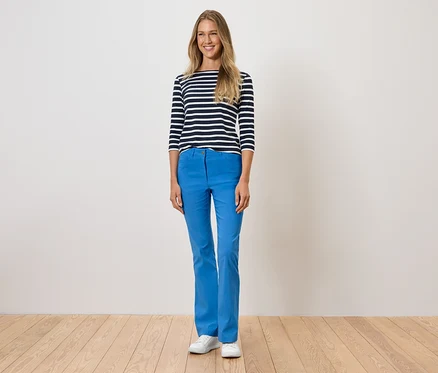 Une femme debout porte un pantalon bleu, un t-shirt rayé et des chaussures blanches.