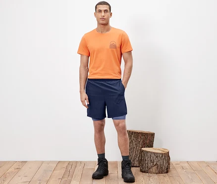 Homme posant en short fonctionnel 2 en 1, t-shirt orange et chaussures de randonnée.