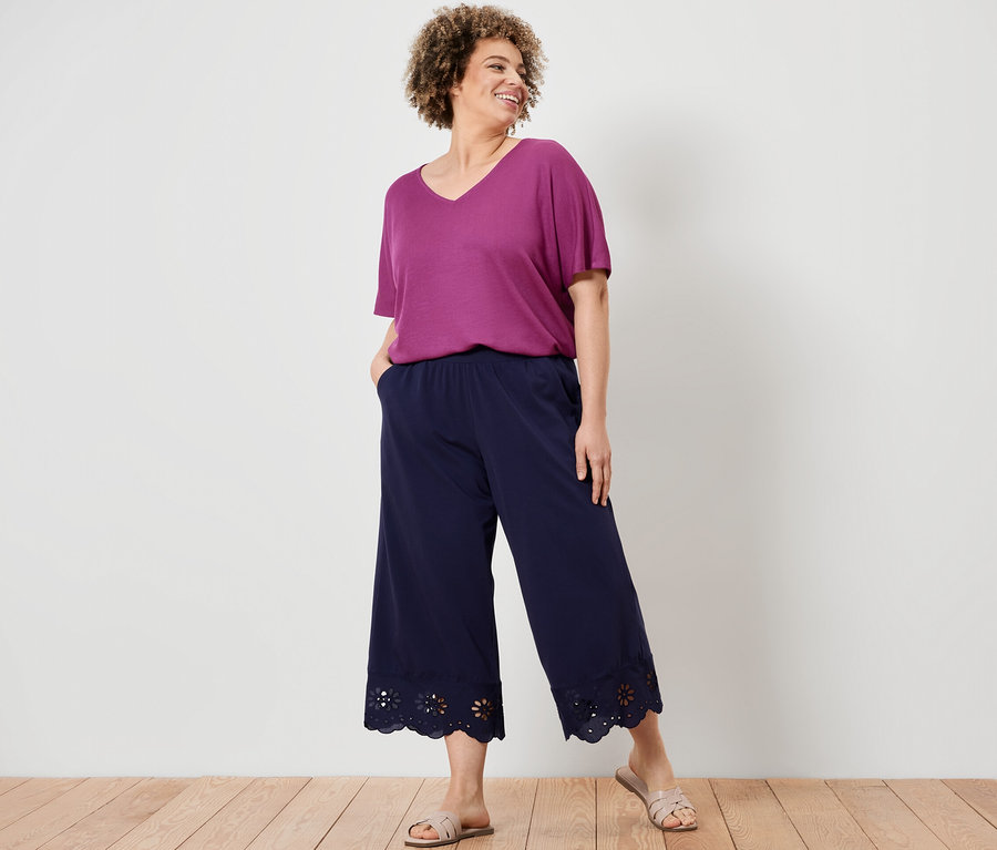 Une femme pose, portant un bas large à broderie et une blouse structurée couleur baies.