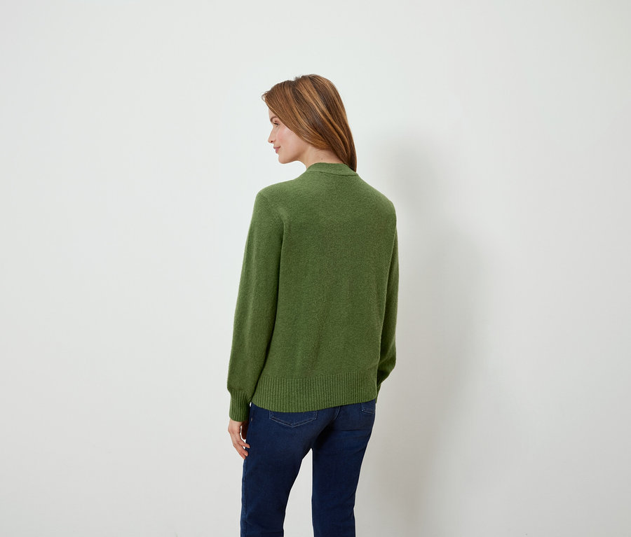 Une femme regardant par-dessus son épaule porte un pull vert et un jean.