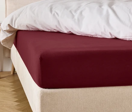 Drap-housse bordeaux sur un lit avec une couette blanche.