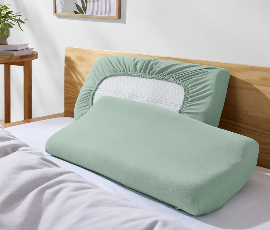 Deux oreillers verts sur un lit avec des draps blancs.