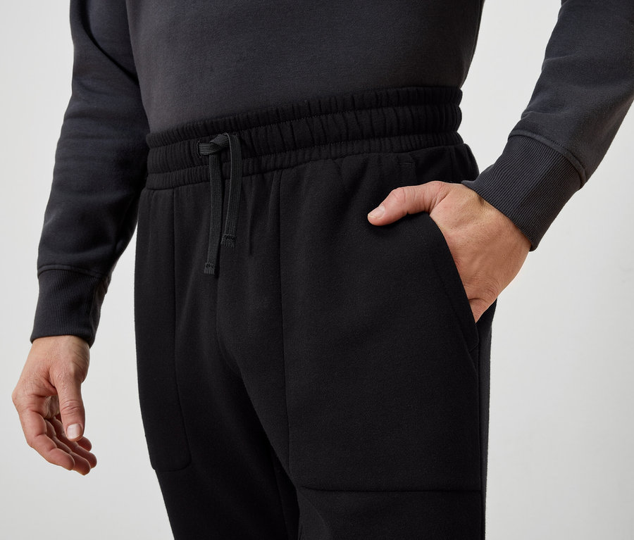 Homme avec la main dans la poche d'un pantalon de survêtement noir.