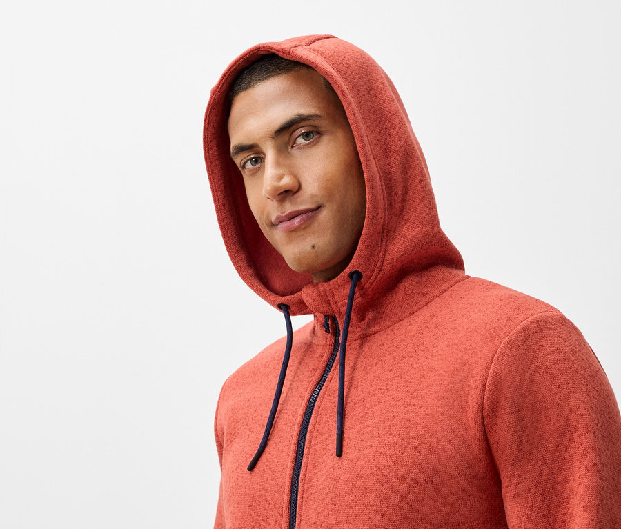 Portrait d'un homme portant un sweat-shirt orange à capuche avec une fermeture éclair bleu marine.