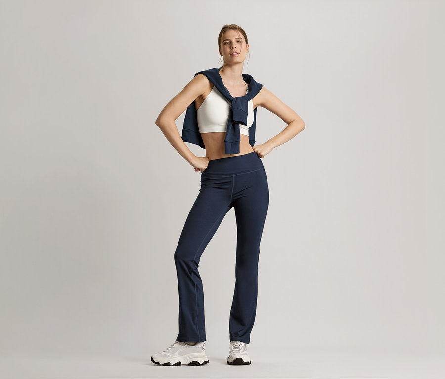 Femme posant avec une veste en sweat bleu marine sur les épaules, un bustier de sport Seamless blanc et un pantalon de sport modelant bleu marine.