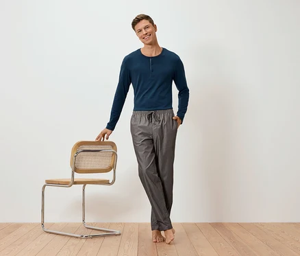 Un homme pose à côté d'une chaise et porte un ensemble pyjama avec un pantalon tissé.