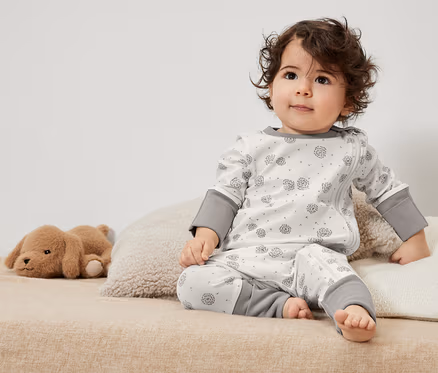 Un tout-petit bouclé est assis sur un lit en 3 pyjamas pour bébé avec un jouet.