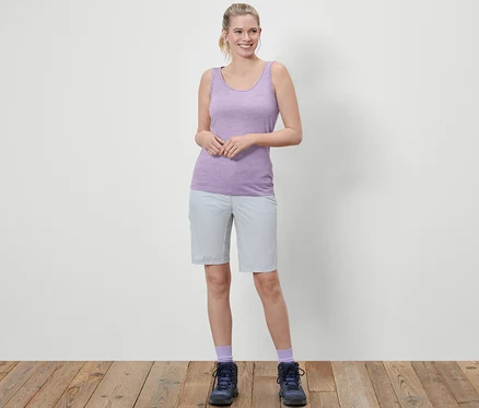 Une femme debout portant un débardeur violet en laine mérinos et un short gris.