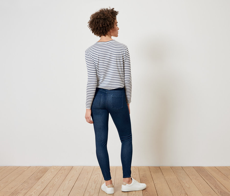 Une femme, vue de dos, porte un t-shirt rayé, un jean foncé et des baskets blanches.