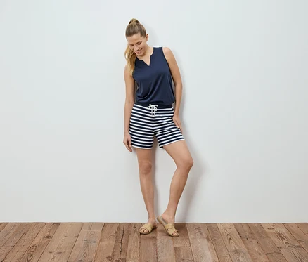 Femme posant devant un mur blanc, portant un haut bleu marine et un short rayé.
