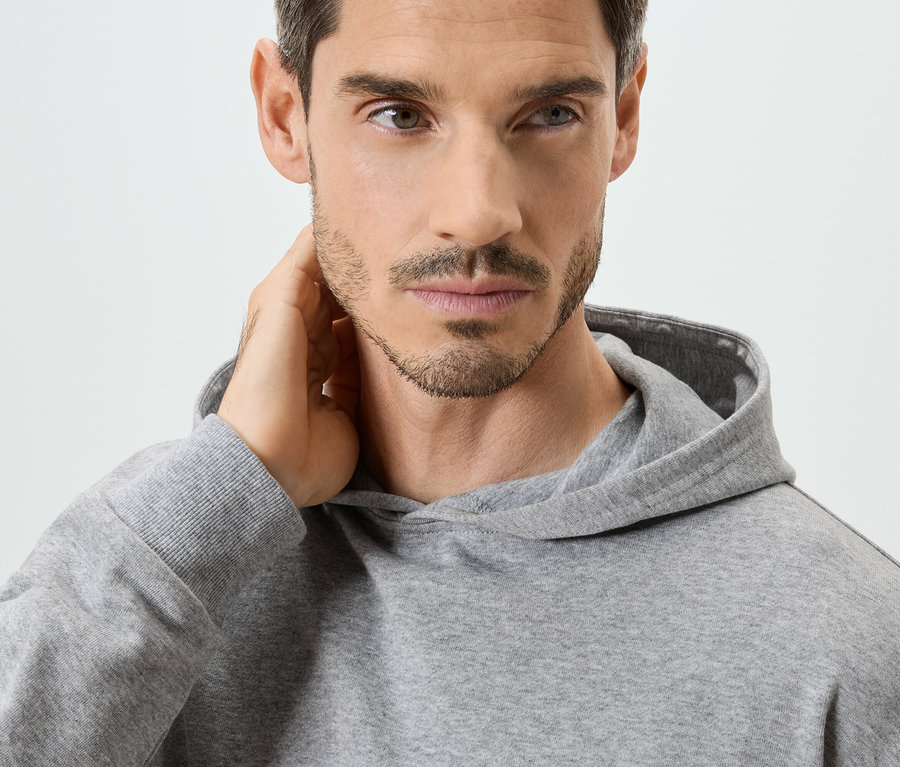 Gros plan d'un homme portant un sweat à capuche gris, la main sur la nuque.