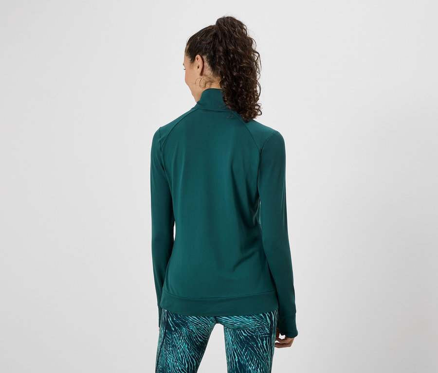 Femme vue de dos portant une veste de survêtement verte et des leggings à motifs sur un fond blanc.