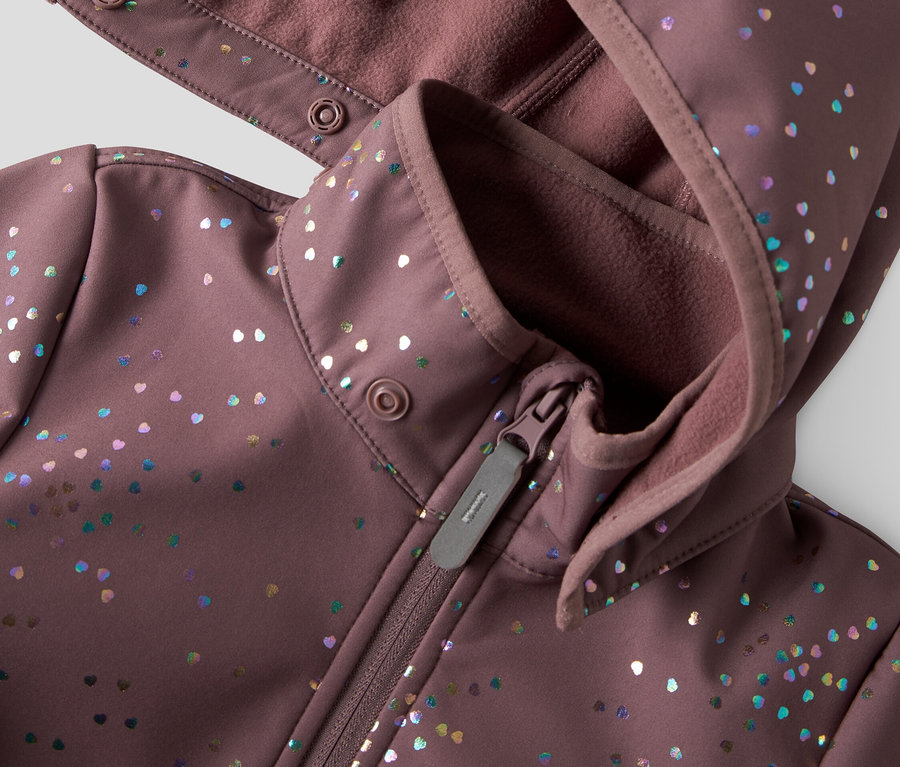 Gros plan d'une veste softshell violette à capuche et fermeture éclair, ornée de points colorés en forme de cœur.