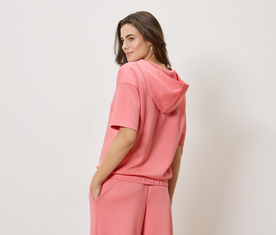 Femme portant un sweat à capuche à manches courtes corail et un short corail assorti.