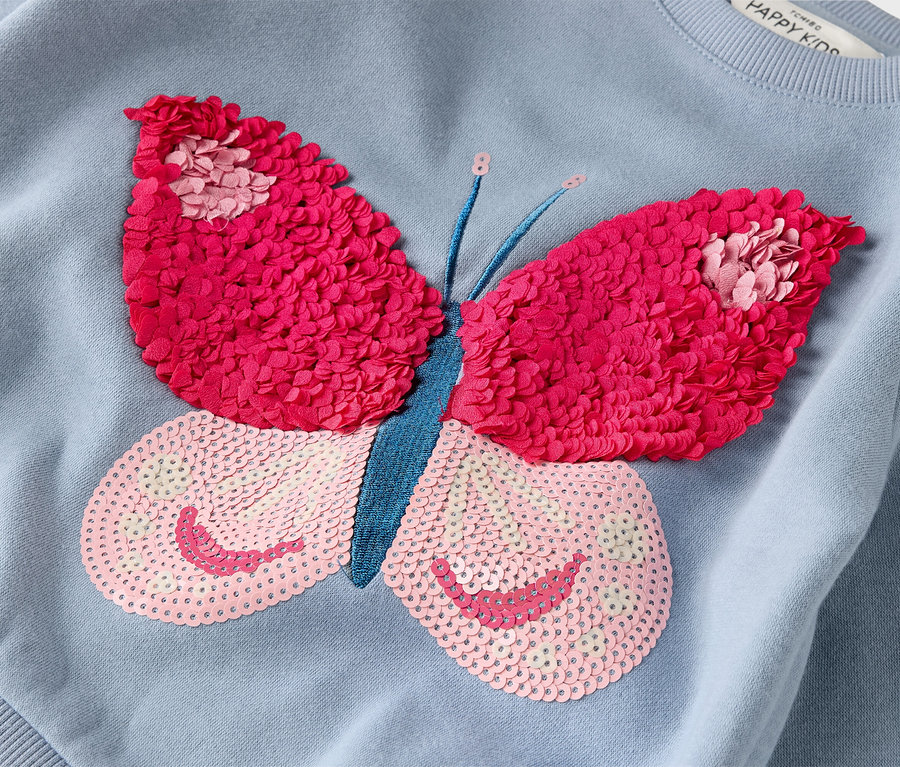 Gros plan sur un sweat-shirt bleu clair orné d'un grand papillon rose et fuchsia.