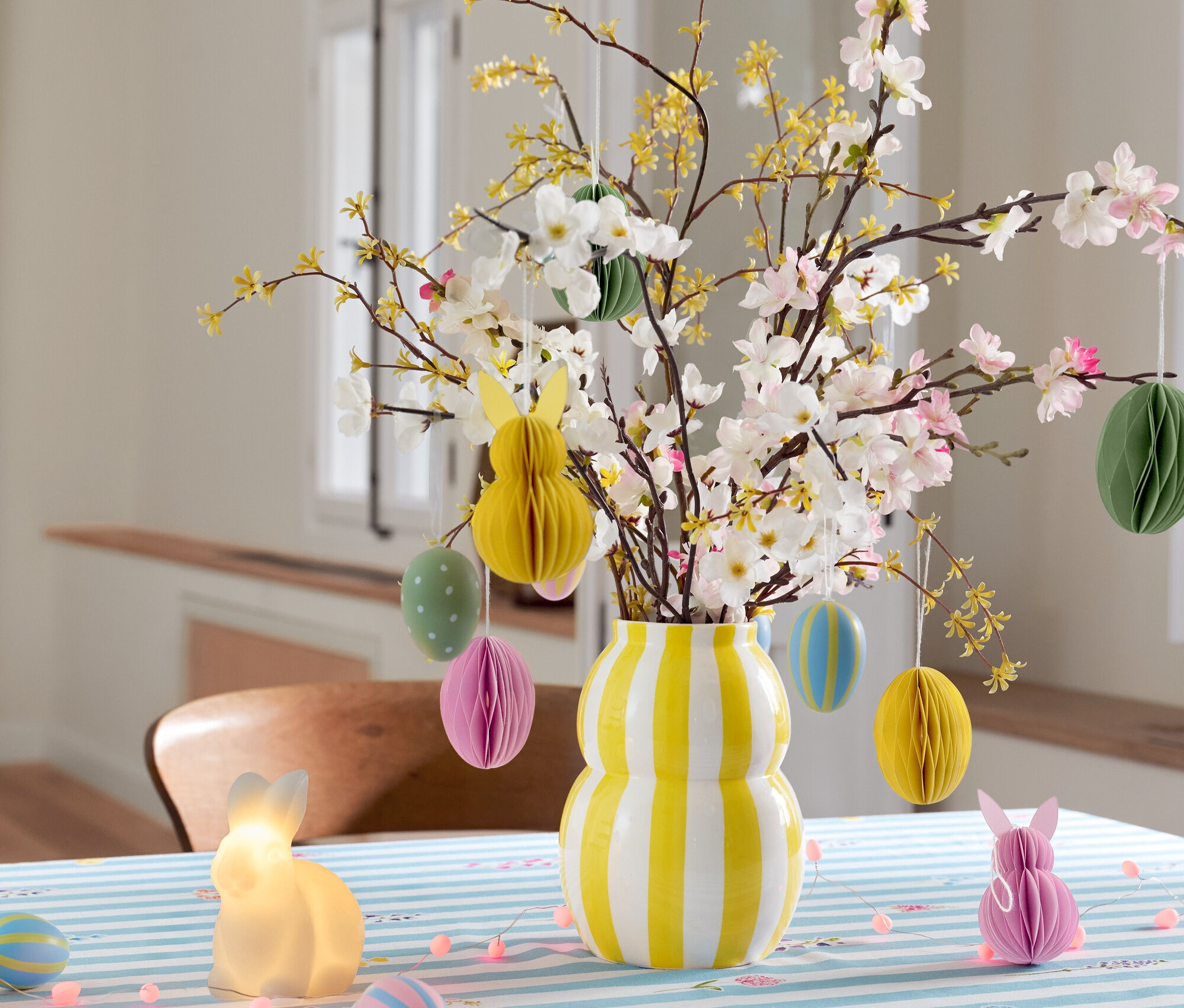 Vase rayé avec des branches et des décorations de Pâques sur une table avec une nappe rayée bleu et blanc.