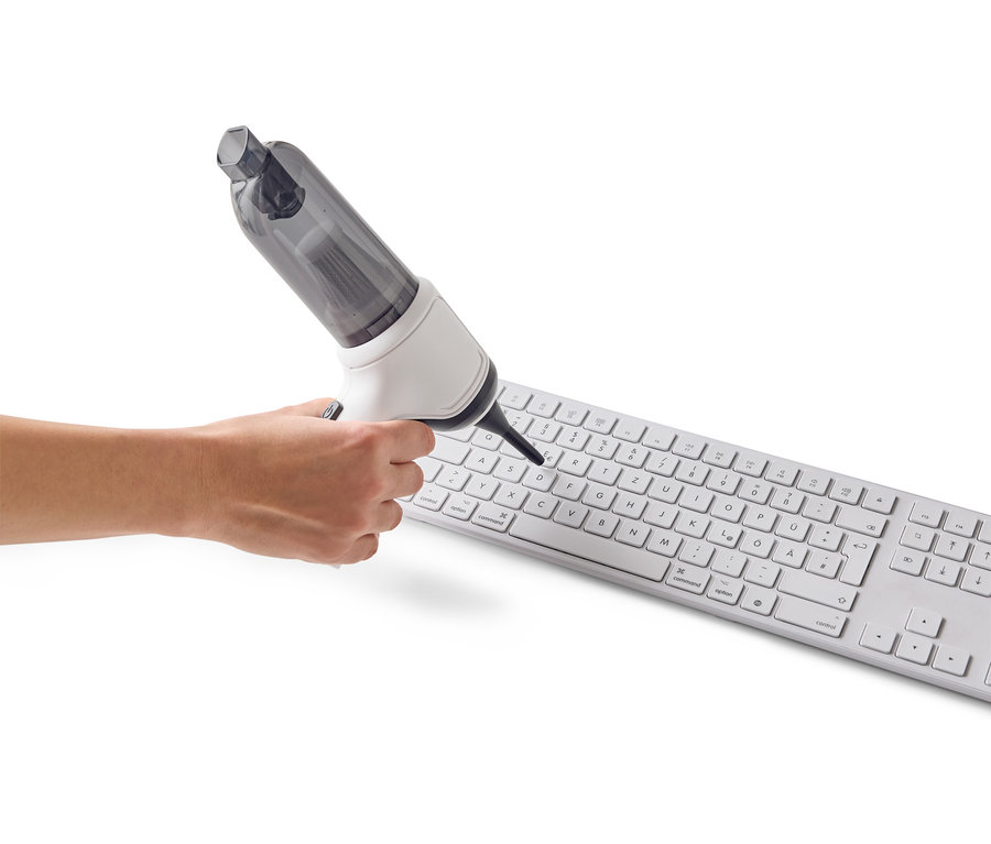 Une main utilise un mini aspirateur pour nettoyer un clavier d'ordinateur blanc.