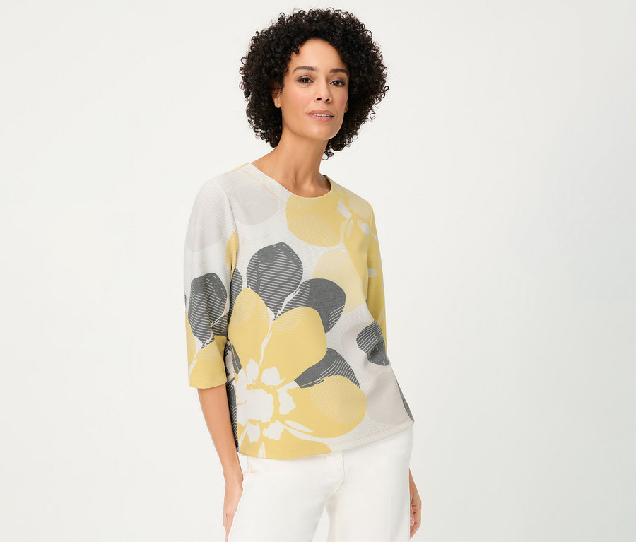 Une femme porte un sweat-shirt Olsen « Ottoman » à fleurs jaunes et grises sur fond blanc.