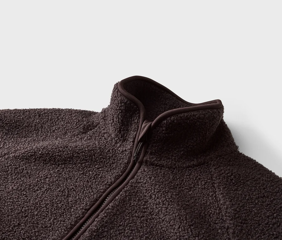 Gros plan d'une veste polaire marron foncé avec fermeture éclair et col montant sur fond blanc.