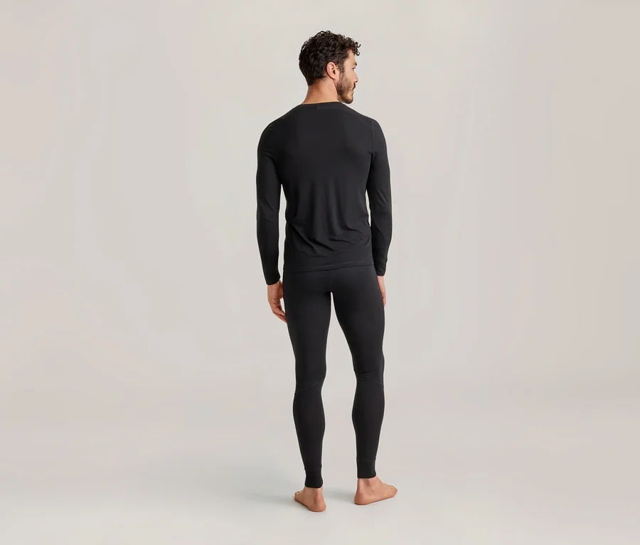 Un homme vu de dos portant des sous-vêtements thermiques noirs composés d'un haut à manches longues et d'un legging sur un fond clair.