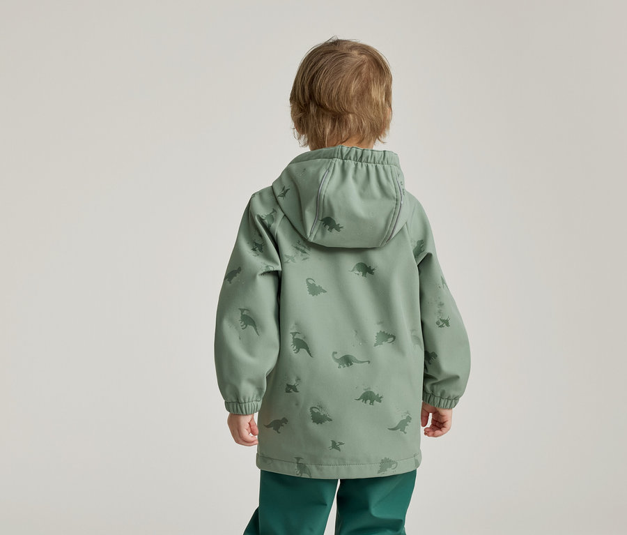 Enfant vu de dos portant une veste à capuche verte à motifs de dinosaures et un pantalon vert sur fond clair.