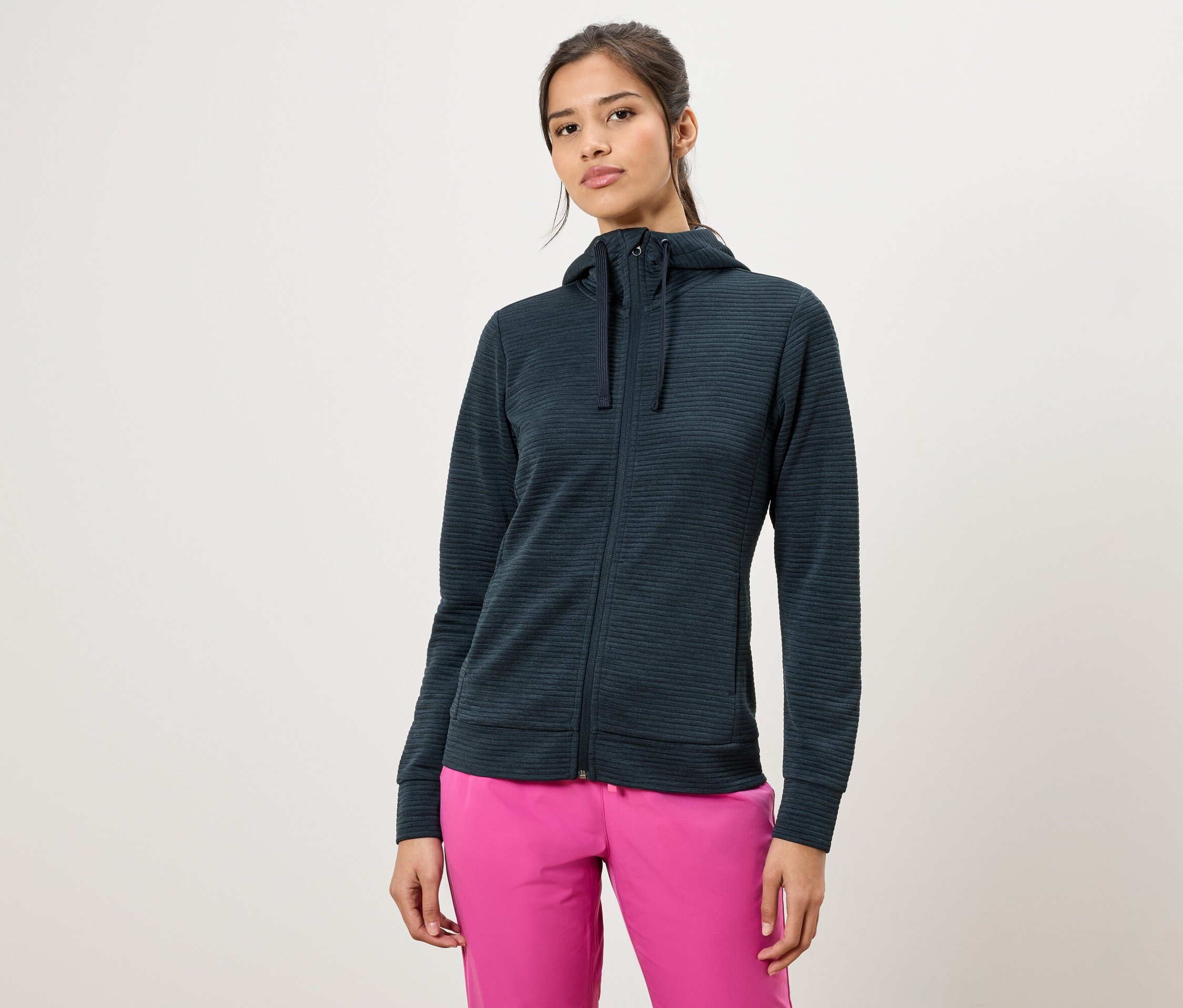 Femme portant un sweat à capuche zippé vert foncé et un pantalon rose.