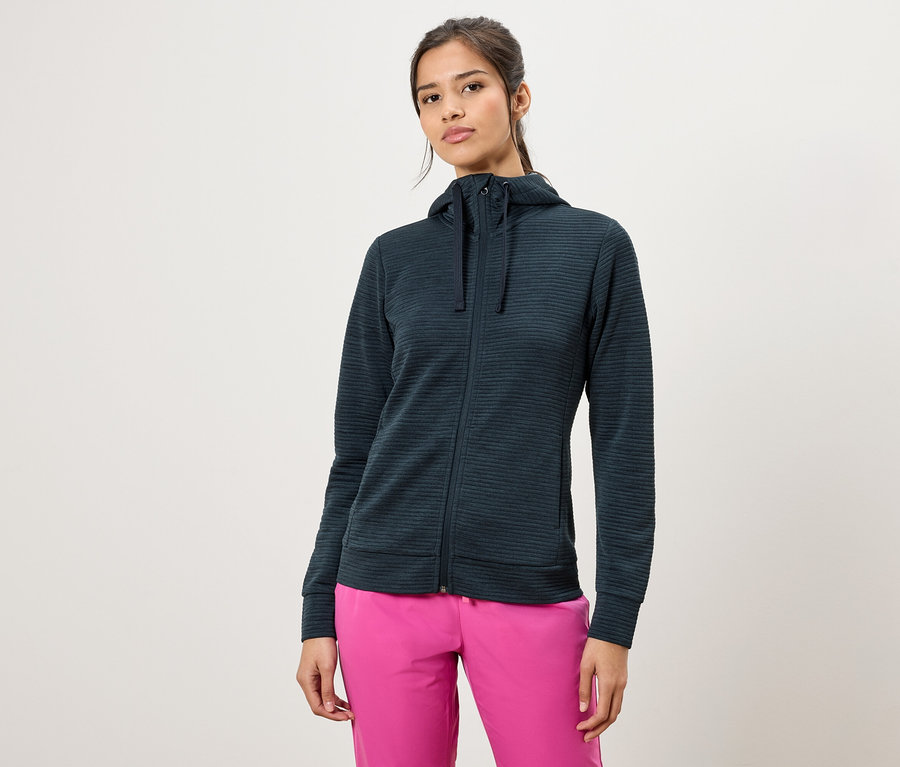 Femme portant un sweat à capuche zippé vert foncé et un pantalon rose.